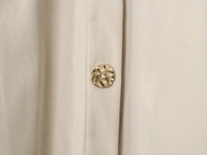 Détail macro d'un bouton en métal martelé doré sur une robe en sergé beige