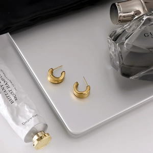 Detail of wide golden C-shaped hoop earrings with a matte finish on a metallic surface