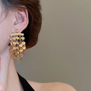 Close-up of golden multi-layer disc tassel earrings worn by a model in soft lighting