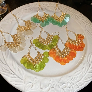 Detail of bohemian tassel earrings with colorful sequins and golden beads on a white tray