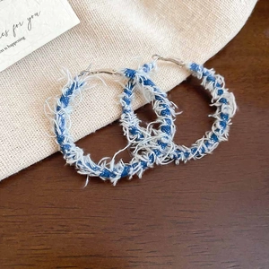 Detailed close-up of blue denim wrapped hoop earrings with frayed fringe texture