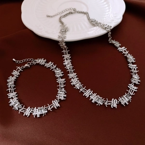 Macro view of silver necklace and bracelet set with square zircon on red fabric