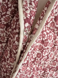 Detailed close-up of metal hook closure on a floral quilted jacket with fine stitching