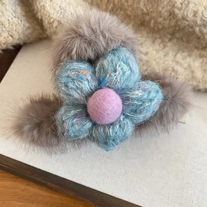 Detailed close-up of a plush gray fur hair claw clip with a blue knit flower design