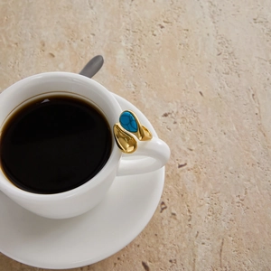 Detail of gold titanium steel ring with turquoise stone on a white ceramic coffee cup handle