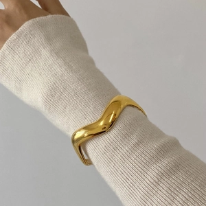 Close-up of 18k gold-plated wavy irregular bangle on wrist showing polished surface