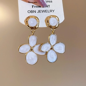Détail de boucles d'oreilles pendantes en forme de fleur dorée et émail blanc sur carte