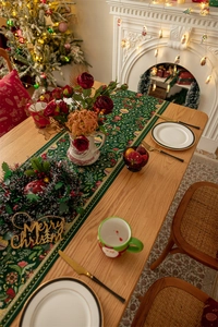 Close-up of green Christmas table runner with red floral pattern and wooden Merry Christmas sign