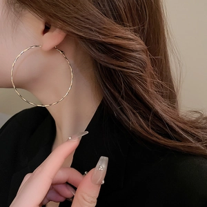 Close-up of model wearing textured gold hoop earrings with minimalist metal design