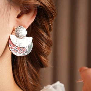Close-up of a silver earring featuring a circular stud and cactus desert scene pendant