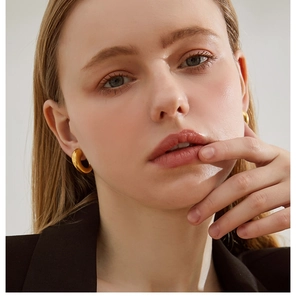 Close-up of model wearing chunky gold hoop earrings with a vintage French horn design
