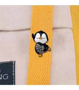 Detail of penguin brooch with rhinestones pinned on yellow ribbon against canvas bag