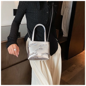 Silver shoulder bag with metallic finish and bow details shown as a crossbody wear