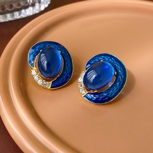 Macro shot of vintage gold earrings with deep blue oval enamel and crystal accents