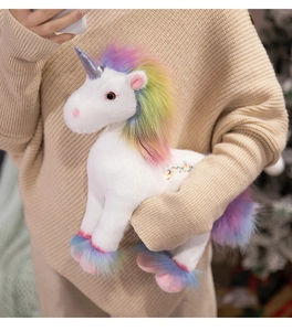 Detail of soft white plush unicorn with rainbow mane and embroidery held by person