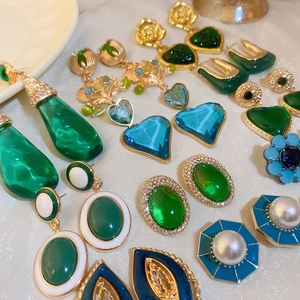 Close-up of vintage gold earrings with green gemstones, pearls and enamel details