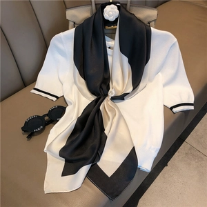 Detail of a chic striped silk scarf tied on a white knit sweater with black sleeve trim