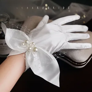 Detail of white bridal satin gloves featuring a luxury bow with pearls and tulle mesh