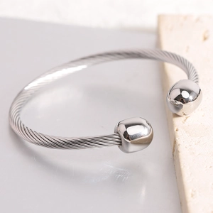 Silver twisted cable cuff bracelet with polished spherical ends on stone background