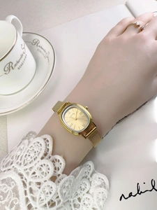 Elegant gold rectangular quartz watch with mesh strap worn while reading a book