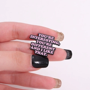 Black enamel pin with pink text featuring Coraline movie quote You are Interesting