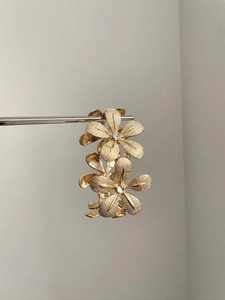 Close-up of golden flower earrings with textured petals and center crystal stone