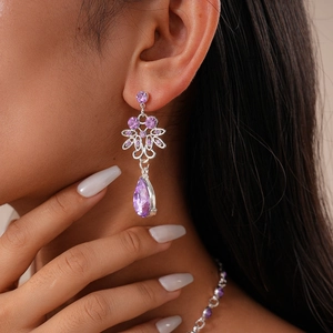 Close-up of model wearing silver flower earrings and necklace with purple teardrop gems