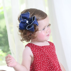 Detailed view of child hair clip with dark blue ribbon bow and white wavy edges