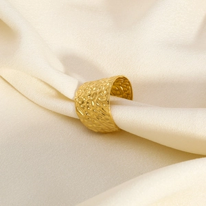 Primo piano di un anello largo martellato placcato oro 18K su elegante seta bianca