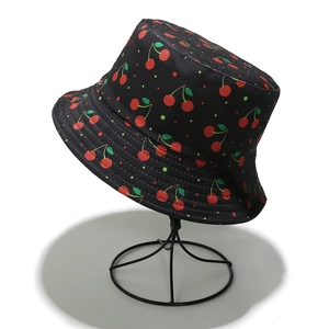 Detail of the black sun bucket hat featuring a vibrant red cherry pattern and cotton texture