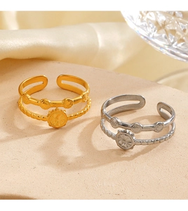 Detail of double-layer geometric rings in 18K gold and silver finishes on beige surface