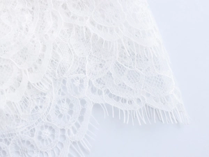 Détail de la broderie en dentelle blanche et texture ajourée sur l'ourlet de la robe