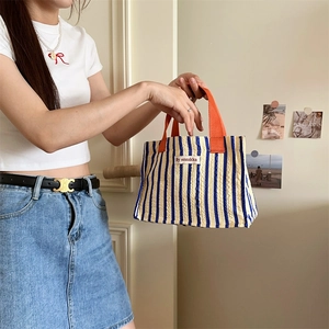 Striped canvas tote bag in blue and white with orange handles shown on a model
