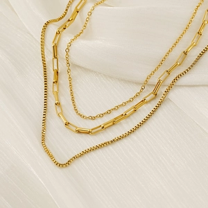 Chic triple-layered gold necklace with cable and box chains on soft white fabric