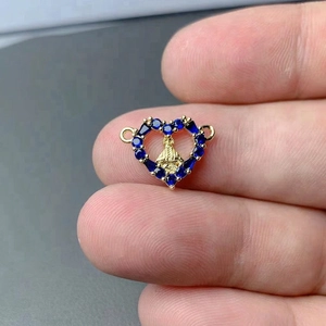 Macro view of a gold heart pendant featuring a religious relief and blue cubic zirconia