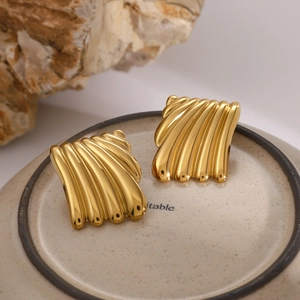 Detail of 18K gold stainless steel square earrings with ribbed texture on ceramic plate