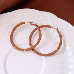 Detail of brown hoop earrings with hammered texture on a decorative white ceramic plate