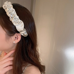 Close-up of champagne satin pleated headband with sparkling rhinestone embellishments