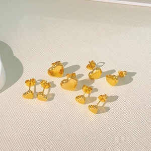 Polished gold heart studs in various sizes displayed on a textured beige surface