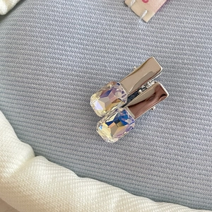 Macro view of metal hair clip with iridescent rectangular crystal on blue fabric