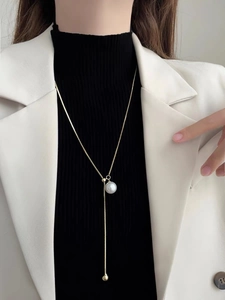 Detailed view of elegant gold Y-shaped pearl necklace worn on a black sweater