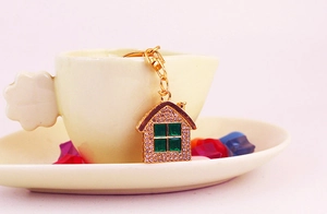 Detailed view of a gold house keychain with green gems on a beige ceramic cup