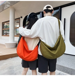 Rear view of model wearing large crescent oxford shoulder bags in orange and olive green