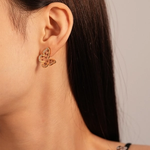 Detailed view of butterfly stud earrings with gold plating and zircons on model ear