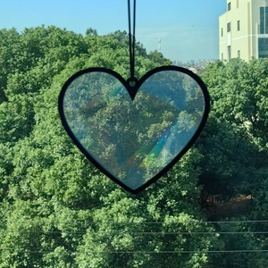 Detail of heart suncatcher glass prism reflecting rainbow light against green forest background