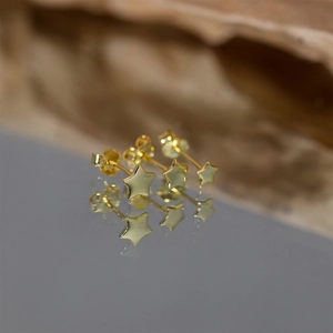 Close-up of gold-plated star stud earrings with butterfly backs on a reflective surface