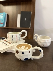 Three handmade irregular ceramic coffee mugs with painted patterns on a wooden desk