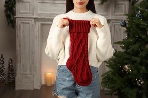 Detail of red knit Christmas stocking with diamond weave pattern held in a festive home
