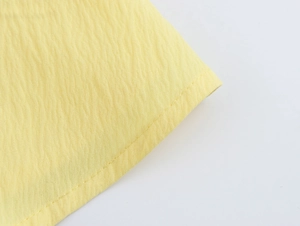 Dettaglio del tessuto giallo con trama plissettata e cuciture precise sull'abito a balze