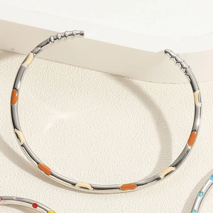 Détail d'un bracelet ouvert argenté avec des points en émail orange et beige sur pierre